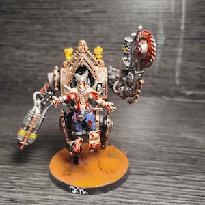 May include: A miniature figure of a cyborg character mounted in a mechanical frame with a large circular saw arm and a projectile weapon arm. The figure features metallic bronze, silver, and blue details with red paint splatters on a round base.