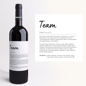Könnte beinhalten: Eine dunkelrote Weinflasche mit schwarzem Verschluss und weißem Etikett. Das Etikett zeigt das Wort "Team" in handschriftlicher Schrift, zusammen mit einer Definition und einer Liste von Namen. Die Flasche ist mit "GREATSY" beschriftet.