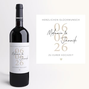 Könnte beinhalten: Eine dunkelrote Weinflasche mit individuellem Etikett. Das Etikett zeigt die Namen "Melanie & Jannik" mit dem Datum "06 26" und dem Text "HERZLICHEN GLÜCKWUNSCH ZU EURER HOCHZEIT". Die Flasche hat einen schwarzen Verschluss und ein "GREATSY"-Etikett.