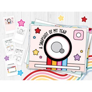 May include: A stack of pink and white paper sheets with a camera design and the text "A Snapshot of My Year." The design includes a rainbow stripe, stars, and Instagram-style icons. Additional sheets with fill-in-the-blank prompts are scattered around.