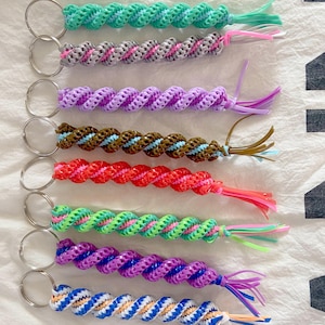 May include: A selection of spiral keyrings in various colours. Each keyring has a unique colour combination, including green, pink, purple, brown, red, and blue. The keyrings are made of a woven material and have a metal ring for attaching keys.