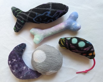 May include: Five plush toys for cats, including a fish, a bone, a moon, a ball, and a mouse. The toys are made of soft, colorful fabric with various patterns.
