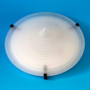 Pode incluir: Uma luminária de teto circular de vidro fosco com um design cônico de ondas concêntricas que se eleva até um ponto central. A cúpula de vidro é fixada por três clipes de metal preto espaçados uniformemente na borda externa.