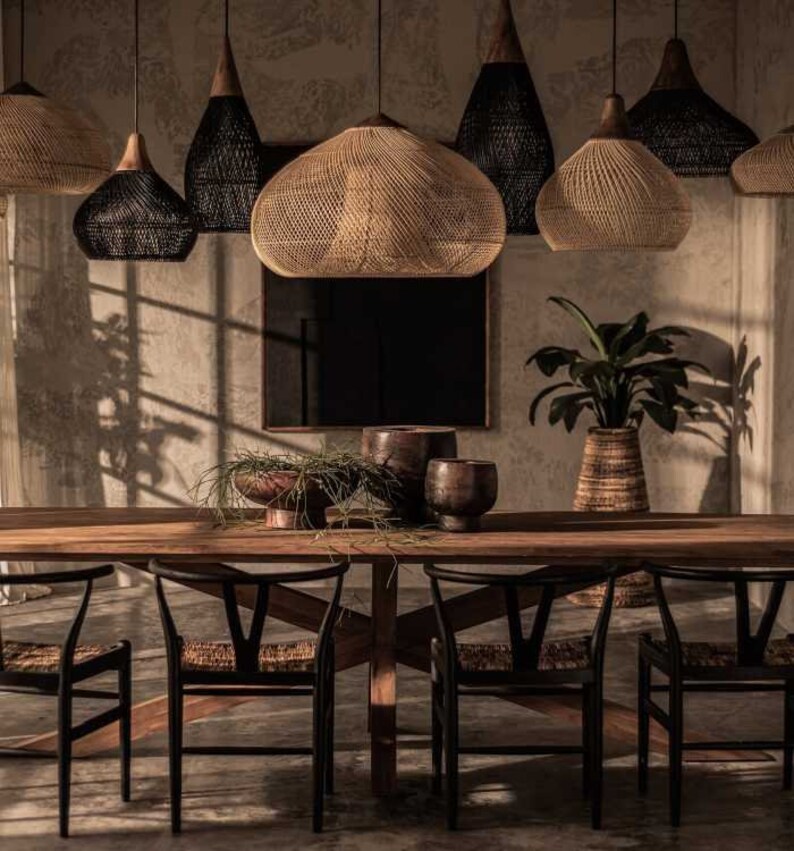 May include: A wooden dining table with four black chairs and woven pendant lights hanging above. The table is set with a vase of greenery and decorative bowls.