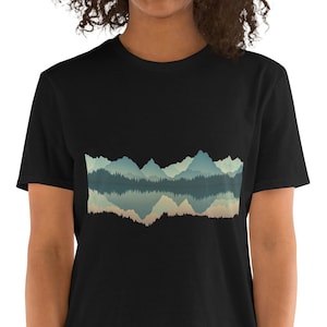 Op de afbeelding: Een zwart T-shirt met korte mouwen met een grafische print van een blauwe en groene bergketen die in het water wordt weerspiegeld.