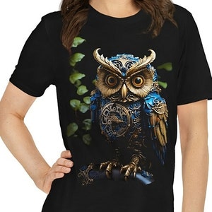 May include: Black t-shirt featuring a graphic of a steampunk owl with gold and blue accents. The owl is perched on a branch with green leaves.