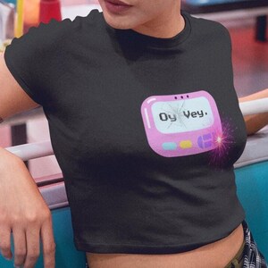 May include: A black crop top with a pink and blue graphic of a digital device with the text "Oy Vey!" on the screen. The graphic has a pink border and a white outline.