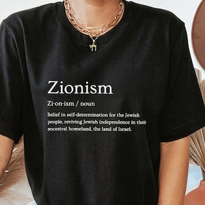 May include: Black t-shirt with the word "Zionism" and its definition printed in white. The definition is: "Zi-on-ism/noun Belief in self-determination for the Jewish people, reviving Jewish independence in their ancestral homeland, the land of Israel."