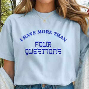 May include: Light blue t-shirt with the text "I HAVE MORE THAN FOUR QUESTIONS" in blue. The text is arched across the top and bottom of the shirt. The word "FOUR" and the word "QUESTIONS" are in a different font.