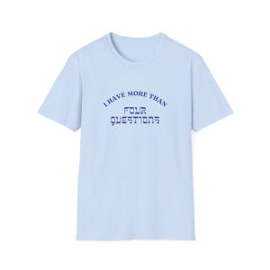 May include: Light blue t-shirt with a crew neck and short sleeves. The shirt features the text "I HAVE MORE THAN FOUR QUESTIONS" in navy blue, arched above the word "QUESTIONS" in a stylized font.