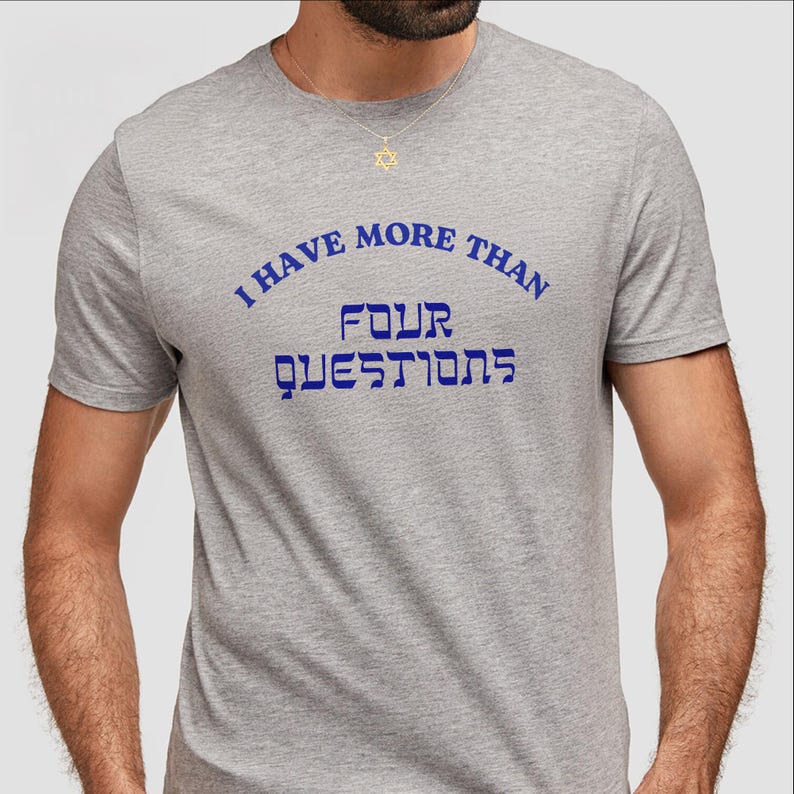 May include: A gray t-shirt with the text "I HAVE MORE THAN FOUR QUESTIONS" in blue. The Hebrew word for "questions" is also printed on the shirt. A gold Star of David necklace is visible.