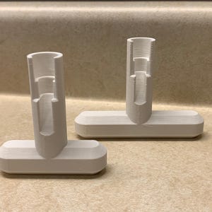 May include: Two white plastic T-shaped stands with a hollow cylinder on top. The stands are designed to hold items upright.