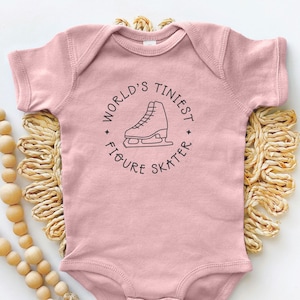 May include: A pink baby onesie with a black graphic of a figure skate and the text "World's Tiniest Figure Skater".