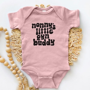 May include: Pink baby onesie with black text that reads "mommy's little gym buddy" in a retro font.
