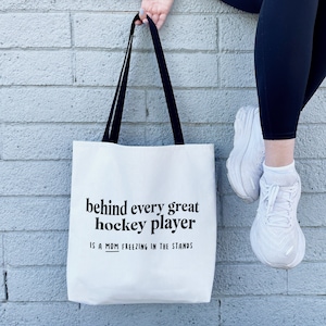 May include: White canvas tote bag with black handles and the text "behind every great hockey player is a mom freezing in the stands".