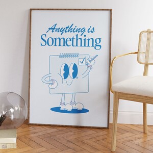 May include: A framed print with a blue illustration of a notepad character with the text "Anything is Something" on a white background.