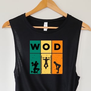 Könnte beinhalten: Schwarzes ärmelloses Muscle-Tanktop mit einem Retro-Grafikdesign. Die Grafik zeigt das Wort "WOD" in einem gelben Kasten, mit drei Silhouetten von Personen, die verschiedene Übungen in grünen, orangefarbenen und gelben Kästen ausführen.