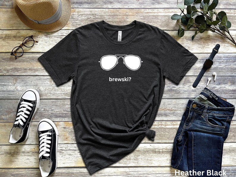 Puede incluir: Una camiseta de color negro jaspeado con un gr&aacute;fico blanco de gafas de sol y el texto "brewski?" impreso en la parte delantera.