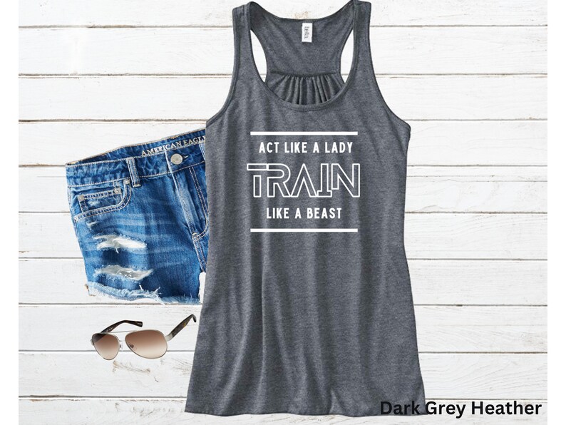 May include: Dark grey heather tank top with white text that reads "Act like a lady, train like a beast".