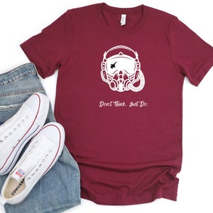 May include: A maroon t-shirt with a white graphic of a pilot wearing a helmet and oxygen mask. The text "Don't think. Just Do." is printed below the graphic.