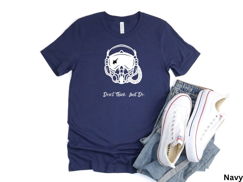 May include: Navy blue t-shirt with a white graphic of a pilot's helmet with a fighter jet in the visor. The text "Don't Think. Just Do." is printed below the graphic.