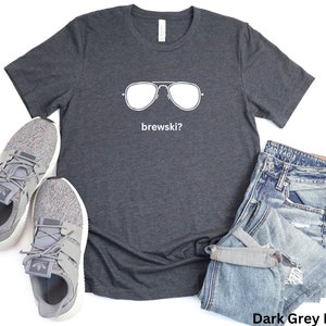 Puede incluir: Camiseta de color gris oscuro jaspeado con un gr&aacute;fico blanco de gafas de sol y el texto "brewskis?"