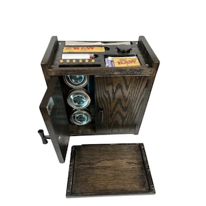 May include: A dark wood storage box with a hinged door and a pull-out tray. The box has a compartment for rolling papers, a small jar, and a lighter. The door opens to reveal three glass jars.