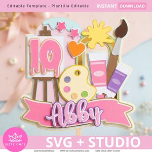 Puede incluir: Un adorno para pastel de papel en capas con temática artística. Presenta una pancarta rosa con el nombre "Abby", el número 10, un pincel, tubos de pintura, una paleta y estrellas. También se incluye el texto "SVG + STUDIO".