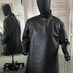 Puede incluir: Una camisa negra acolchada de cuello alto con mangas largas. La camisa está en un maniquí.