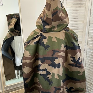 Könnte beinhalten: Camouflage-Kapuzencape mit langem, fließendem Design. Die Kapuze ist aus einem weichen, bequemen Stoff gefertigt und verfügt über eine Kapuze mit Kordelzug.