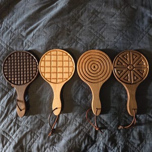 May include: Four wooden paddle-shaped trivets with different carved designs. The trivets are made of dark and light wood and have leather hanging straps.