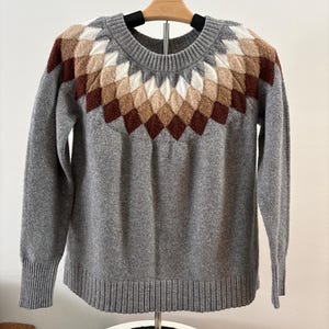 May include: A gray sweater with a brown, beige, and white geometric pattern around the neckline.