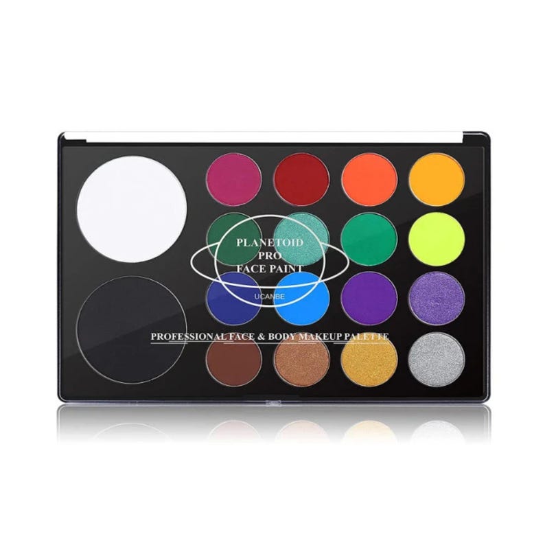 May include: A professional face and body makeup palette with a black case. The palette contains a large white circle, a black circle, and 16 vibrant colors, including shades of pink, red, orange, yellow, green, blue, purple, and silver. The text "PLANETOID PRO FACE PAINT" is printed on the palette.