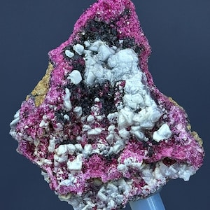 Könnte beinhalten: Ein Cluster aus rosa und weißen Kristallen auf einer dunkelbraunen Matrix. Die Kristalle sind klein und haben eine raue Textur. Die Matrix ist unregelmäßig geformt und hat eine raue Oberfläche.