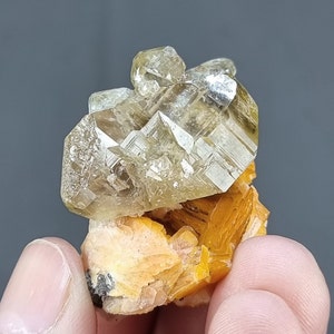 Könnte beinhalten: Ein Cluster aus klaren, facettierten, gelben Calcitkristallen auf einem Bett aus orangefarbenen Calcitkristallen.