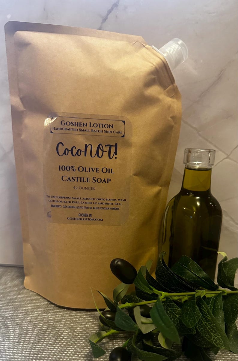May include: A brown pouch with a label that reads "GOSHEN LOTION HANDCRAFTED SMALL BATCH SKIN CARE Coconot! 100% OLIVE OIL CASTILE SOAP 42 OUNCES"  To use: Dispense small amount onto hands, wash cloth or bath puff. Lather up and rinse well. Ingredients: Olea Europaea (Olive) Fruit Oil, Water Potassium Hydroxide. GOSHEN IN GOSHENLOTION.COM. A clear glass bottle of olive oil is next to the pouch.