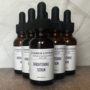 K&ouml;nnte beinhalten: Sechs bernsteinfarbene Glasflaschen mit schwarzen Tropfern, gef&uuml;llt mit einer klaren Fl&uuml;ssigkeit. Die Flaschen sind mit wei&szlig;em Text beschriftet, der "Goshen Lotion", "Handcrafted Small Batch Skin Care", "Brightening Serum", "One Ounce" und "Brightening Serum" lautet.