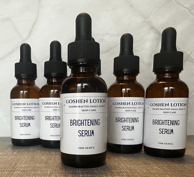 K&ouml;nnte beinhalten: F&uuml;nf bernsteinfarbene Glasflaschen mit Tropfern, jede gef&uuml;llt mit einer klaren Fl&uuml;ssigkeit. Die Flaschen sind mit "Goshen Lotion Handcrafted Small Batch Skin Care Brightening Serum One Ounce" beschriftet.