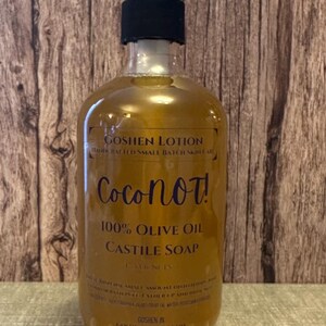 May include: A clear amber glass bottle with a black pump dispenser filled with a golden liquid. The bottle has a label that reads "Goshen Lotion", "Handcrafted Small Batch Skincare", "CocoNot!", "100% Olive Oil Castile Soap", "Coconut", and "Goshen IN GoshenLotion.com".