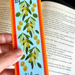 May include: A blue and orange bookmark with a design of olive branches and olives. The bookmark has the text "10&cent;" and "l'oliva" printed on it.