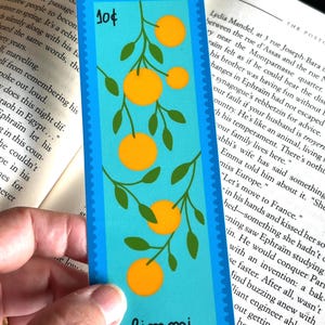 May include: A blue bookmark with a whimsical illustration of a branch of orange citrus fruit with green leaves. The bookmark has a white border and the word "limoni" in a white cursive font. The bookmark also has a blue stamp with the number "10&cent;" in white.