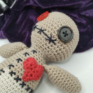 Puede incluir: Una mu&ntilde;eca vud&uacute; de crochet con un coraz&oacute;n rojo en el pecho, ojos de bot&oacute;n negro y nariz de bot&oacute;n rojo.