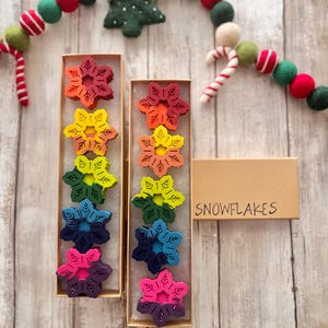 Puede incluir: Dos cajas de crayones de copo de nieve de color arco&iacute;ris. Las cajas est&aacute;n etiquetadas con "SNOWFLAKES".