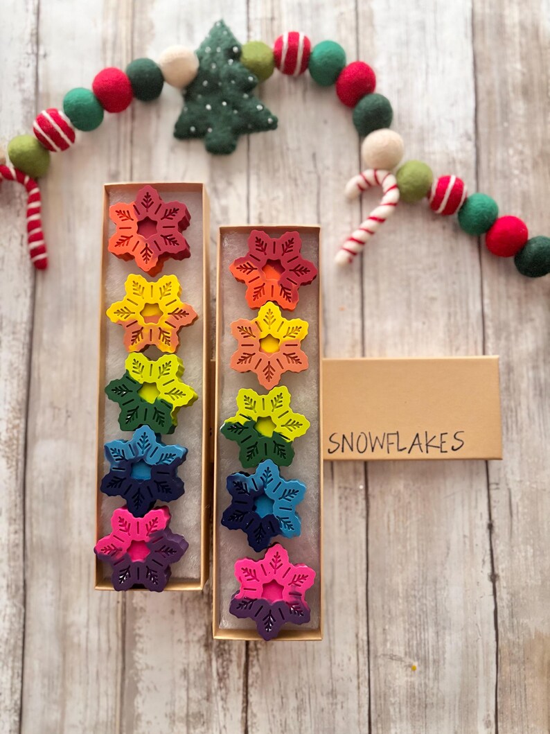 Puede incluir: Dos cajas de crayones de copo de nieve de color arco&iacute;ris. Las cajas est&aacute;n etiquetadas con "SNOWFLAKES".
