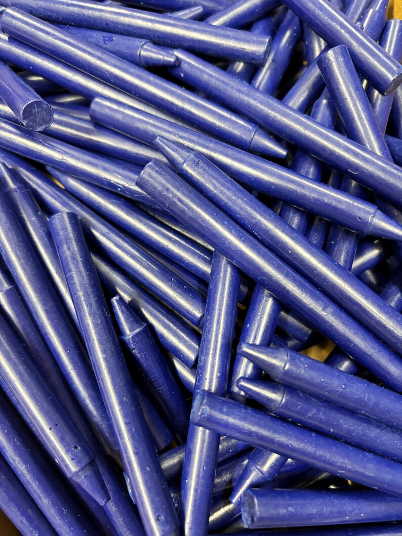 May include: A pile of deep blue crayons, all lying together in a jumbled heap. The crayons are all the same size and shape, and they have a smooth, glossy finish.