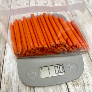 May include: A large bag of orange crayons on a digital kitchen scale that reads 1.00 oz.
