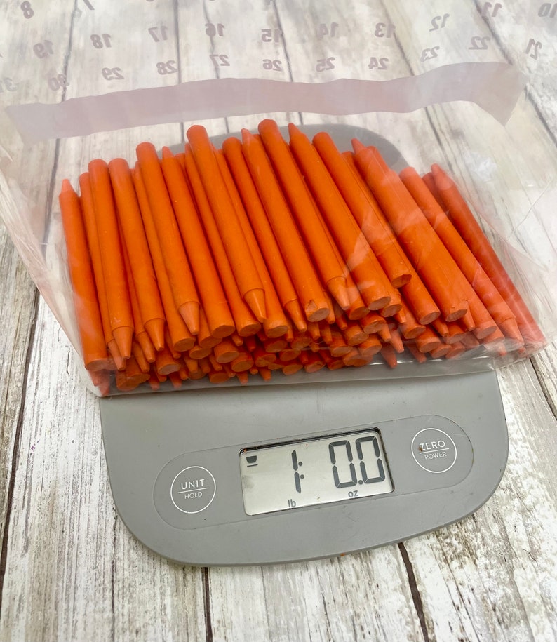 May include: A large bag of orange crayons on a digital kitchen scale that reads 1.00 oz.