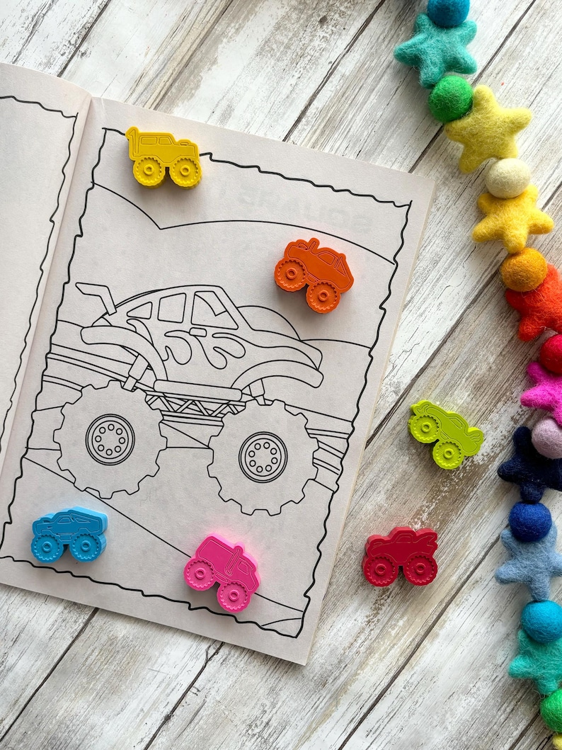 May include: A colouring book page featuring a monster truck illustration.  The page is surrounded by small toy monster trucks in various colours, including yellow, orange, red, pink, blue and green.