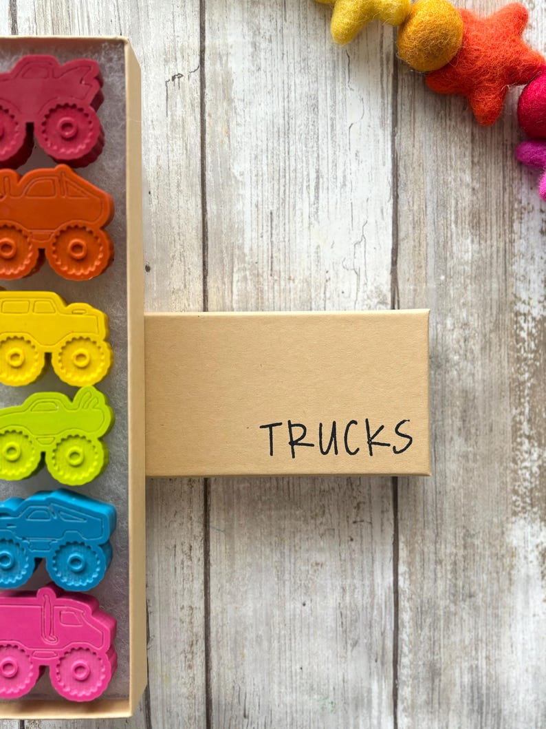 May include: A box of colourful monster truck shaped crayons. The box is labelled "TRUCKS".