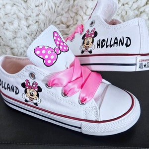 Pode incluir: T&ecirc;nis Converse brancos com cadar&ccedil;os de fita rosa e um design de Minnie Mouse. Os t&ecirc;nis s&atilde;o personalizados com o nome "Holland" em ambos os lados.